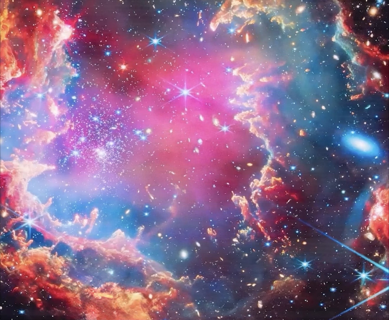 A vivid cosmic illustration of pink, blue and golden nebula clouds, stars and distant galaxies.